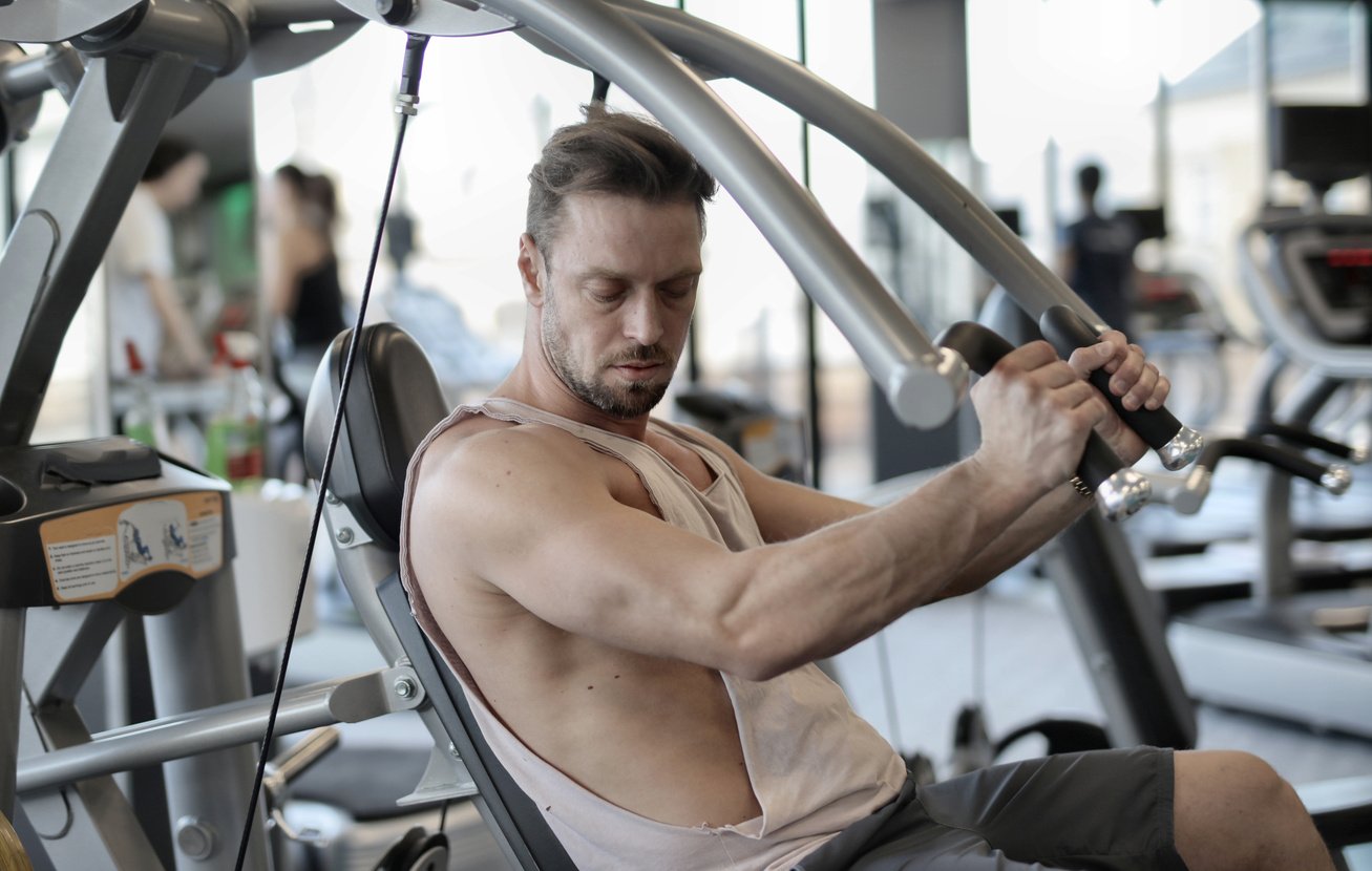 Fit male bodybuilder exercising with metal machine in gym